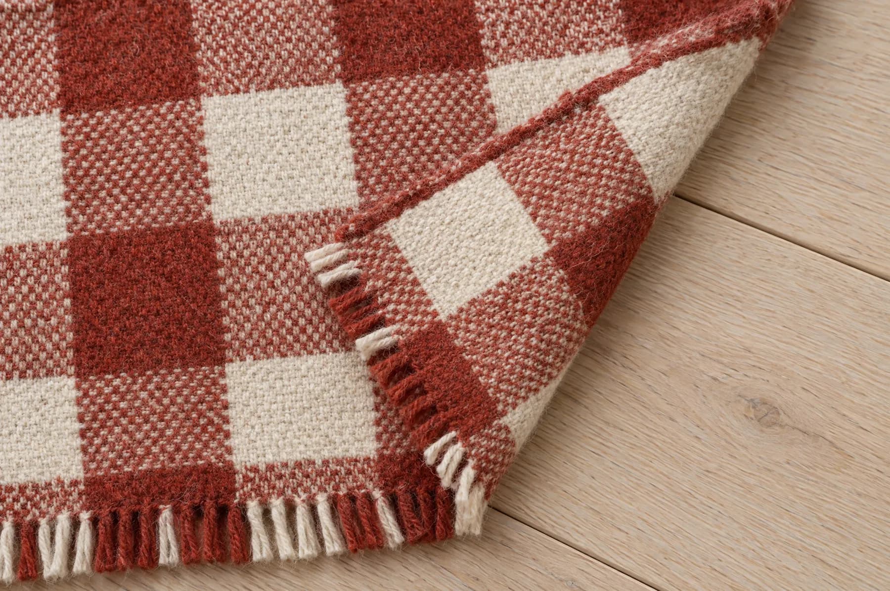 The corner of a russet red and cream block check throw, folded back on itself.